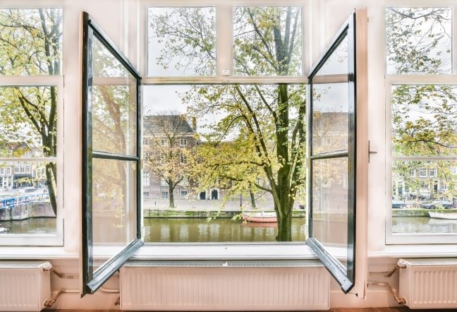 Fotografía de ventana de un hogar abierta, vista exterior a un lago con arbolada.